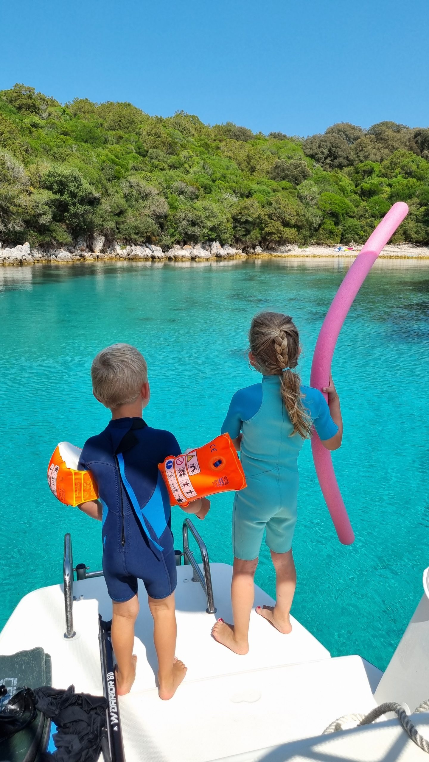 Zwei Kinder mit Schwimmflügeln im türkisfarbenen Wasser einer Felsbucht an der kroatischen Küste