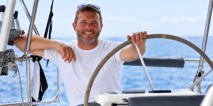 Pablo Schmahl lächelt am Steuer eines Segelboots während eines Flottillentörns in Griechenland