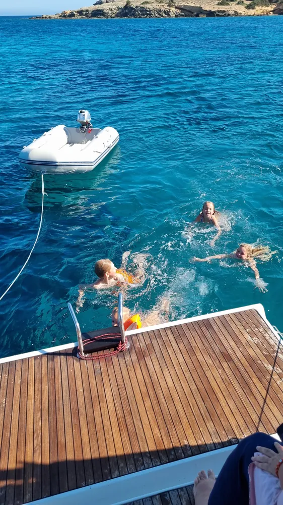 Familie schwimmt hinter dem Heck einer Segelyacht in der Ankerbucht
