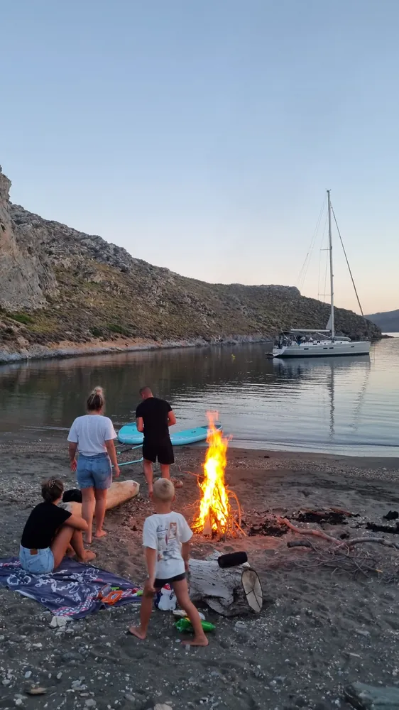 Familien am Lagerfeuer am Strand, im Hintergrund eine Segelyacht